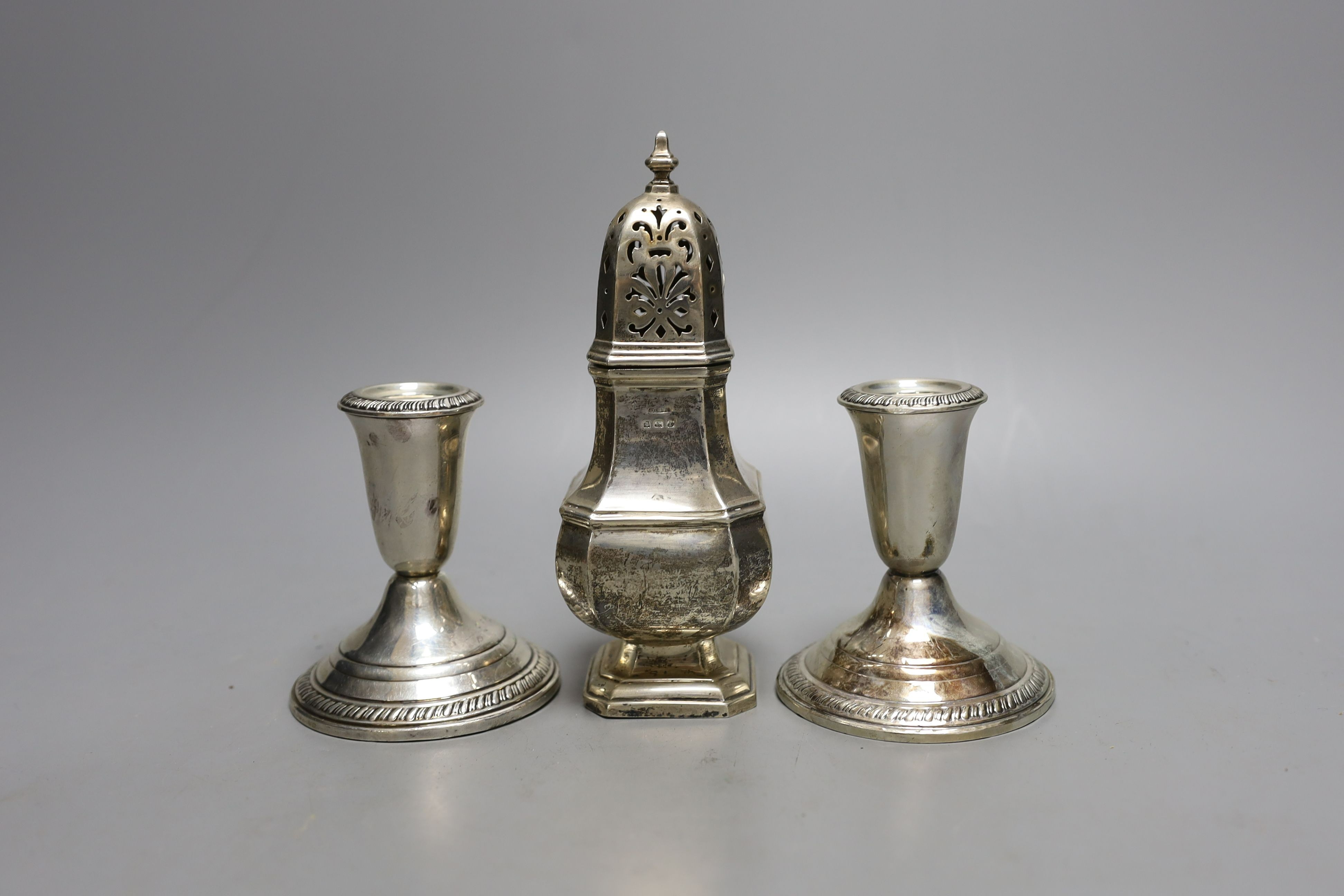 A modern pair of sterling mounted dwarf candlesticks, 92mm and a George V silver sugar caster, 16.5cm, 157 grams.